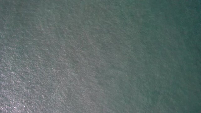 A calm water surface with fine gentle ripples, displaying a soft muted teal color and subtle shimmer.