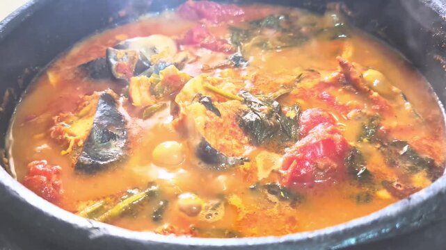 Authentic Brazilian Surubim fish Moqueca boiling in a traditional clay pot. A rich, steaming seafood stew with tomatoes, herbs, and dend&ecirc; oil.