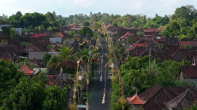 Aerial view of traditional village in Bali with penjor lining the street, surrounded by lush tropical greenery and traditional houses in Kecamatan Tegallalang, Bali, Indonesia.