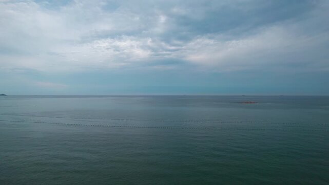 A tranquil seascape with calm water stretching to the horizon under an overcast sky, with gentle surface ripples and distant faint land hints.