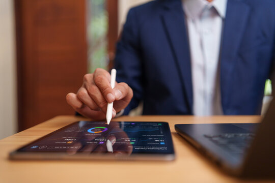 Businessman using stylus on tablet displaying a financial analytics dashboard, reviewing charts, data and performance metrics for business analysis, reporting, planning and digital finance strategy.