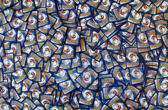 Pokemon cards scattered in a large pile across the surface, showing iconic blue card backs, pokeball logos, natural soft shadows, and vibrant details of popular collectible tabletop game decks.