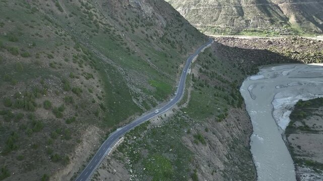 Aerial view of car on a winding road through a rocky Himalayan canyon with a rushing river in Lahaul Valley India shot by a drone
