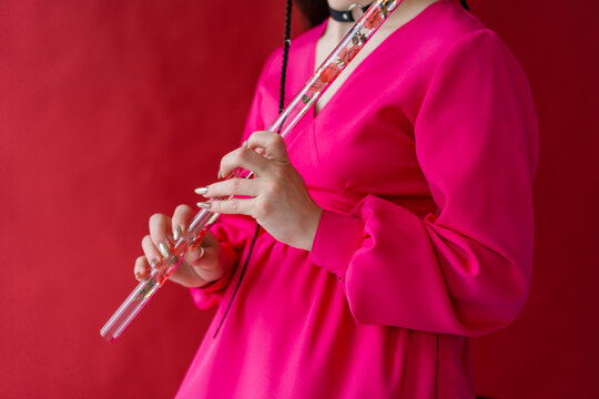 Woman in pink dress on red background playing music on beautiful glass pipe