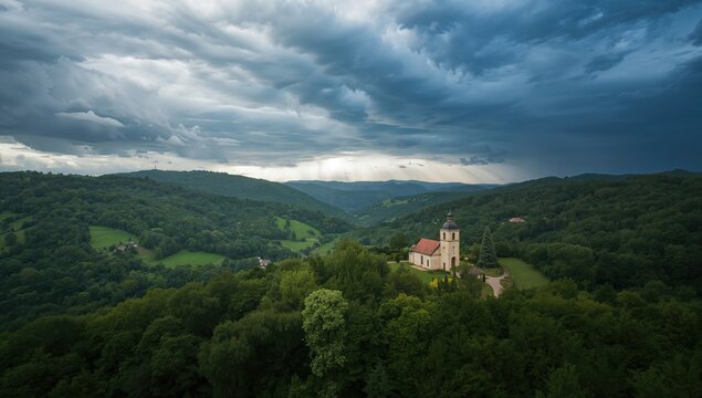 Picturesque Church on a Hill Surrounded by Lush Green Forest and Dramatic Clouds