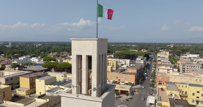 Aerial closeup of the beautiful civic tower of Sabaudia, in the province of Latina, in Lazio, Italy, a rationalist building of the 1930s topped by the Italian flag, seen from above the town centre.