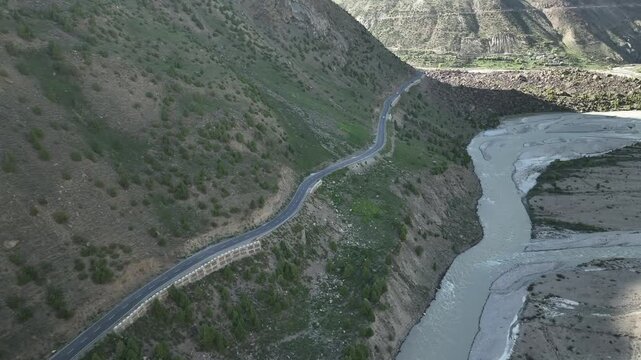 Aerial view of white car driving along a mountain road carved into a steep hillside in Lahaul Valley India shot by a drone
