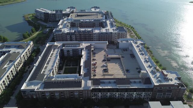 Sprawling apartment complexes accompany open air parking facilities beside North Lake in suburb DFW. Shingled rooftops contrast against glistening open reservoir surfaces, Coppell, Texas