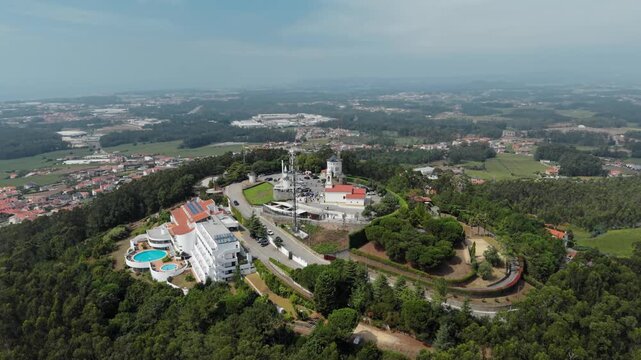 Aerial view of Capela de Sao Felix and Santuario da Senhora da Saude de Laundos on a hilltop surrounded by dense forest and a hotel with a swimming pool in Laundos, Porto, Portugal.