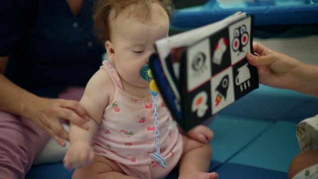 Baby with a pacifier looking at a black and white book for visual development and early learning under adult supervision