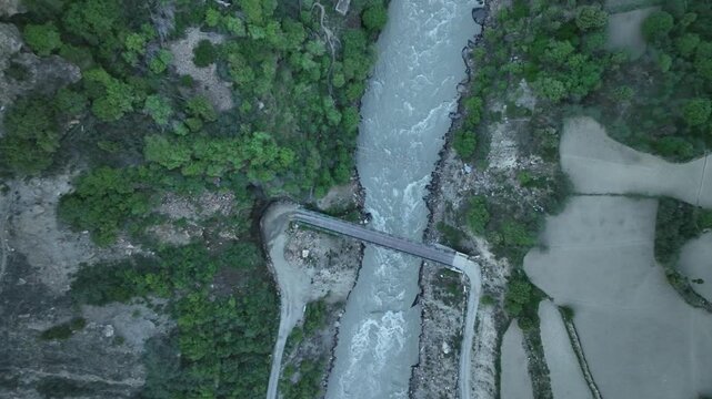 Aerial view of suspension bridge over a mountain river Bhaga, crossing whitewater rapids in a rocky canyon near Jispa Lahaul Valley. shot by a drone flying in himalayan mountains

