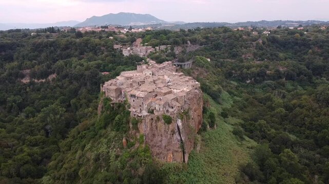 Aerial view of the historic village of Calcata Vecchia perched on a dramatic volcanic cliff surrounded by dense green forests in Calcata Vecchia, Lazio, Italy.