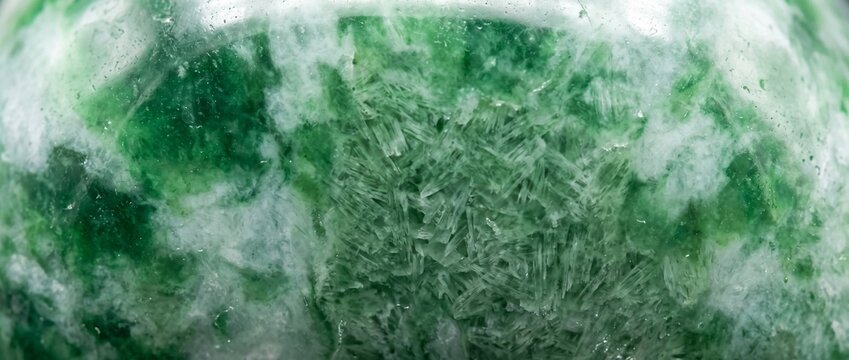 Extreme close-up frontal polished jadeite surface with mottled green translucency and microscopic fibrous crystal structure