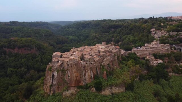 Aerial view of the historic hilltop village of Calcata Vecchia with stone houses perched on a cliff above a lush green valley in Calcata Vecchia, Lazio, Italy.