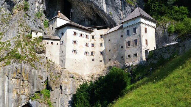 Ancient Predjama Castle With A Woman In Blue Dress Standing Over Viewpoint In Slovenia. Aerial Pullback Shot