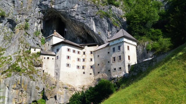 Woman Stands In Front Of Predjama Castle In Slovenia. Historic Castle Architecture And Surrounding Natural Landscape. Aerial Pullback Shot