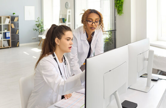 Doctors team use computer for patient records. Colleagues review data in clinic, ensuring healthcare records, diagnostics and collaboration streamline workflow. Teamwork and tech improve care.
