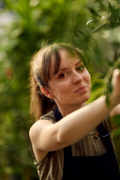 Young Woman Gardener Tending Plants in Greenhouse Portrait Showing Careful, Confident Small-Business Vibe