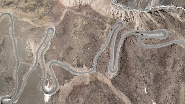 Aerial view of cars driving on loops on multi-tiered switchback road system on a steep rocky mountainside at Shinku La Pass Zanskar shot by a drone flying over loops in himalayas manali leh highway
