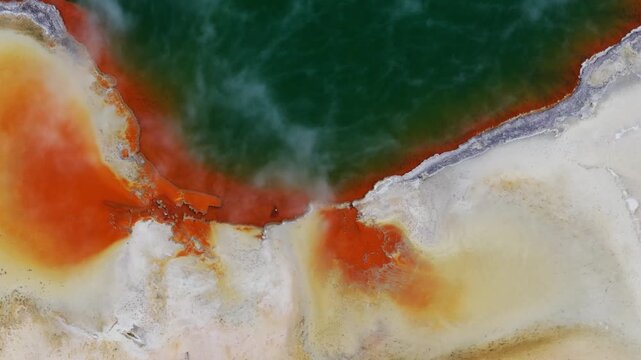 Abstract aerial view of a geothermal pool near Rotorua, New Zealand, with deep green water, vivid orange mineral staining and creamy deposits forming a dramatic natural color composition.