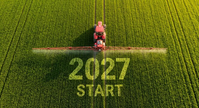 Tractor spraying green field with '2027 start' marked on ground.