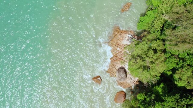 Smooth aerial top-down shot highlighting textured coastal rocks, gentle ocean waves, and tropical forest, ideal for destination marketing, documentaries, and relaxation visuals.