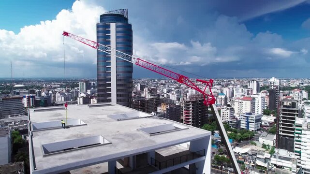 High-angle aerial drone shot orbiting right around a building under construction with a red telescopic crane, revealing the Bella Vista commercial skyline in Santo Domingo