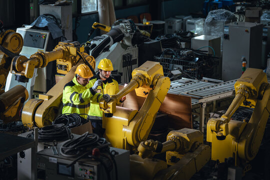 Industrial Maintenance Technicians Inspecting a Yellow Robot Arm among Automated Machinery on a Busy Manufacturing Floor