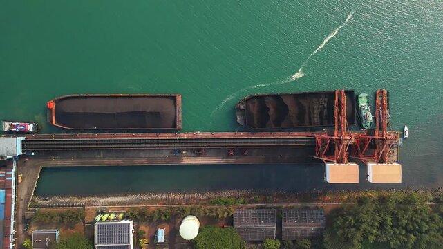 Aerial view of coal barges being loaded at an industrial terminal with conveyor belts and storage facilities