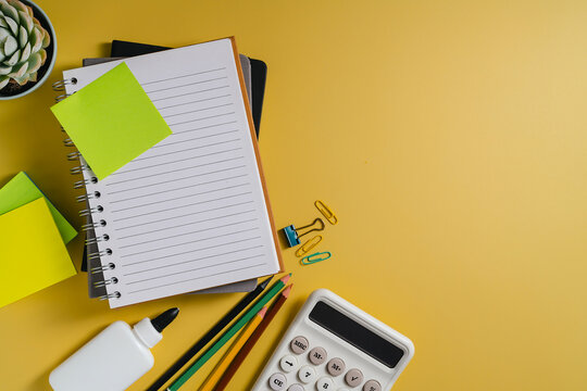 Education study work space flat lay with notebook, stationery and calculator on yellow background with copy space