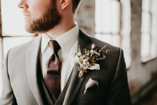Groom in tailored gray suit with textured boutonniere on lapel for wedding portrait background and formal menswear styling