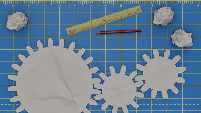 Paper gears and crumpled ideas on a blue cutting mat with ruler