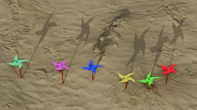 Colorful pinwheels spinning on sandy beach with shadows
