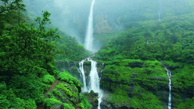 4K Aerial shot of Nanemachi waterfall flowing from mountain cliff during heavy rain in Western Ghats, Maharashtra, India. Beautiful waterfall surrounded by monsoon clouds and lush green forest. 