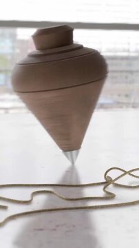 Classic wooden spinning top balanced on its metal tip with string nearby