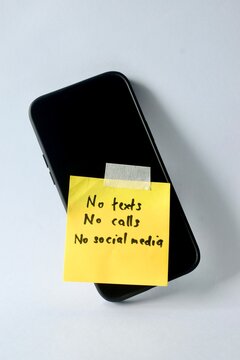 A smartphone lies flat on a white surface with a yellow note taped to the screen reading "No texts, No calls, No social media," showcasing a digital detox concept.
