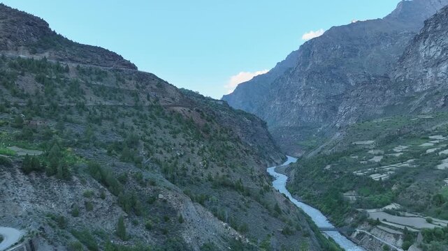 Aerial view of deep river canyon showing a bridge and farm terraces on the cliffs in Lahaul Valley India shot by a drone flying over the Bhaga river in Himalayan mountains
