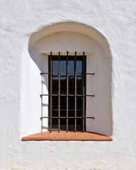 Obraz premium Mediterranean arched stucco window with iron bars and terracotta sill for architectural background, facade design, travel imagery and minimal interior decor