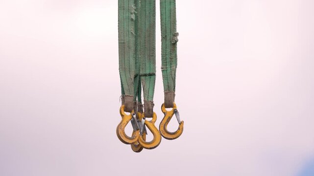 Construction works. Worker prepares to lift equipment using hooks and slings in a construction site. A worker stands on a construction site holding equipment. The worker is ready to use hooks and slin