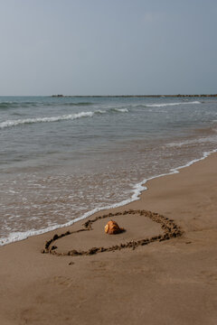 Vertical heart drawn in sand with seashell near ocean waves