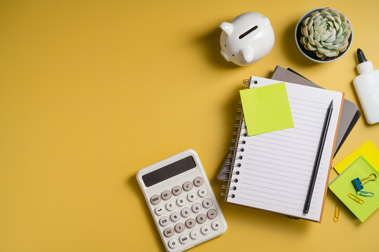 Personal finance planning with piggy bank, calculator and notebook on yellow background with copy space