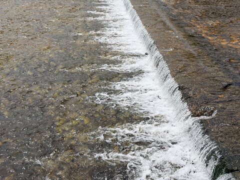 浅い川の堰から流れ落ちる水と白い泡が広がる河川風景｜川,堰,流水,水しぶき,川底