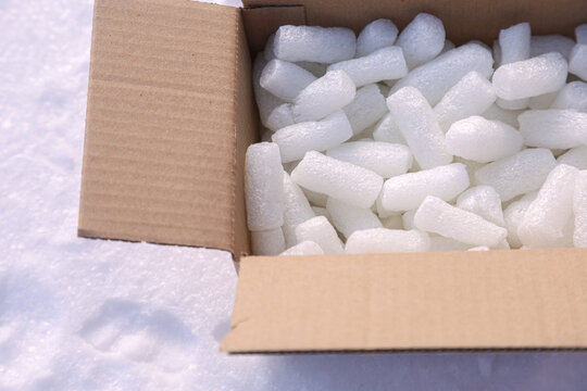 White styrofoam packing peanuts in open cardboard box on snow