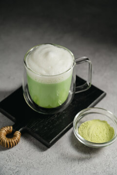 Matcha latte with frothy milk and green tea powder in glass cup. Healthy food, nutrition and antioxidant on dark background with copy space