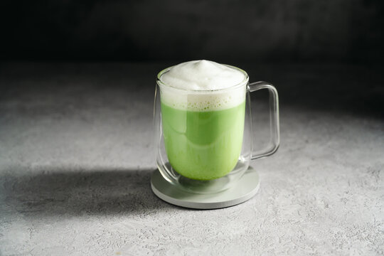 Matcha latte with frothy milk and green tea powder in glass cup. Healthy food, nutrition and antioxidant on dark background with copy space