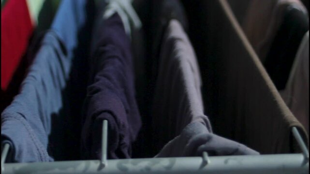 Drying clothes hang closely together on sturdy metal frame indoors. Dark clothes absorb gentle light in calm minimal room. Practical clothes concept illustrates smart domestic space saving.