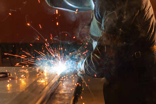 Side view of industrial welder using torch on metal with sparks