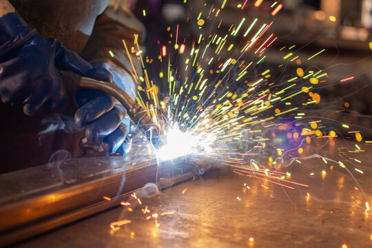 Close up of gloved hands welding metal with torch and bright sparks