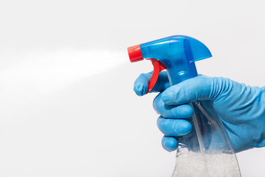 Hand in blue rubber glove holding a blue and red spray bottle releasing a fine mist of liquid with detergent, sanitizer
