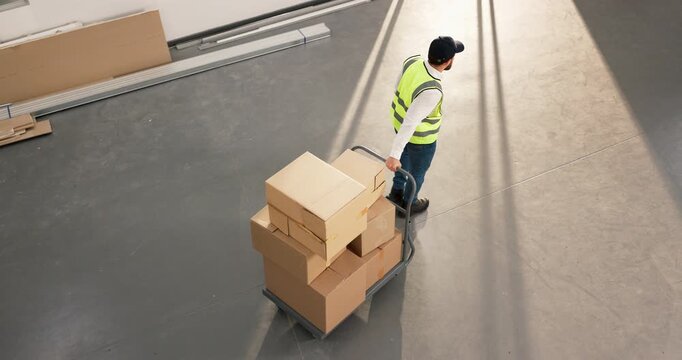 Man, boxes and trolley at depot for logistics, fulfillment and supply chain for stock delivery. Above person, walking or cardboard at warehouse with shipping, dispatch and cargo for distribution
